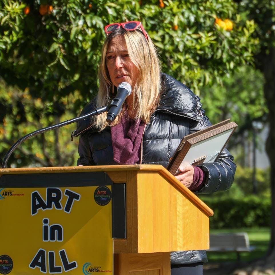 Woman standing in front of a podium with the words "Art in ALL" in front of it